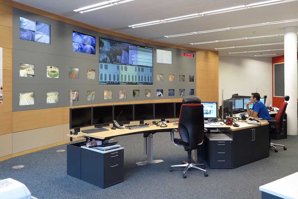 Multi-screen operations room with desks and monitoring displays.